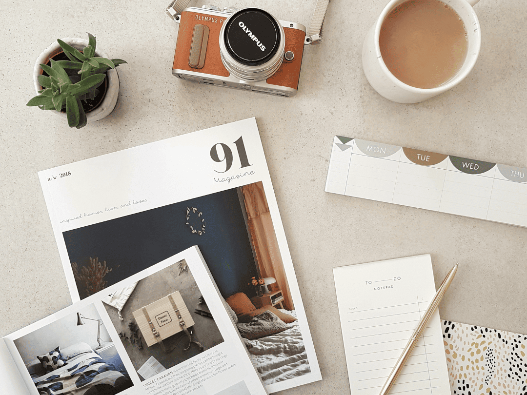 Biurko z gazetą, aparatem, kawą i notatnikiem.